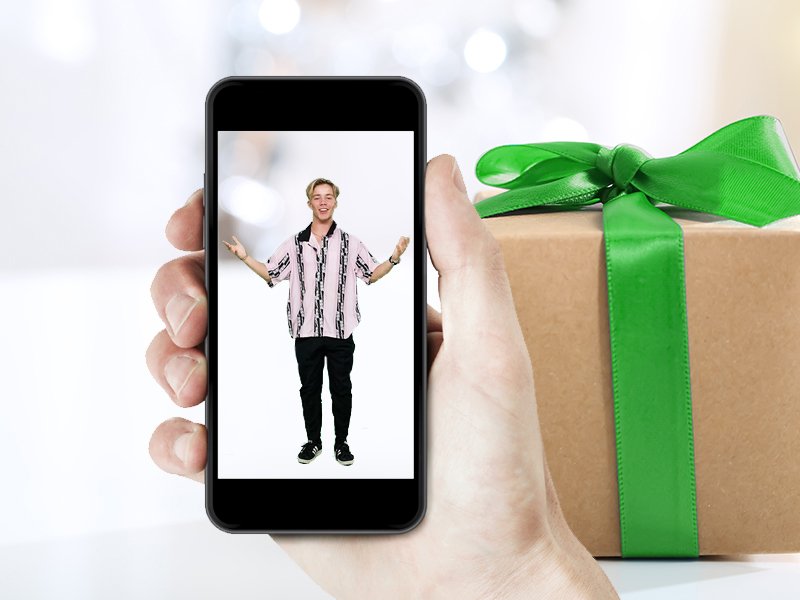 Hånd holder mobil med mann på mobil med gave i bakgrunn