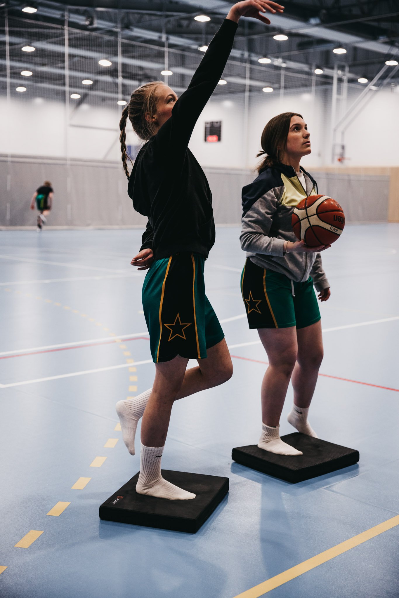 To unge jenter ikledd grønn shorts trener basket og forebygger skader på svarte balanseputer