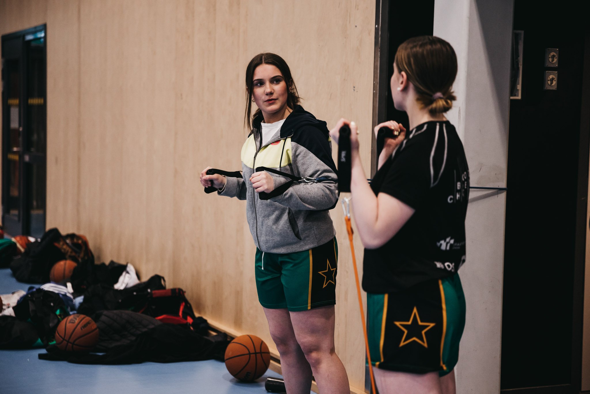To jenter i tenårene snakker sammen mens de trener skadeforebyggende med elastiske bånd i Skjetten basket