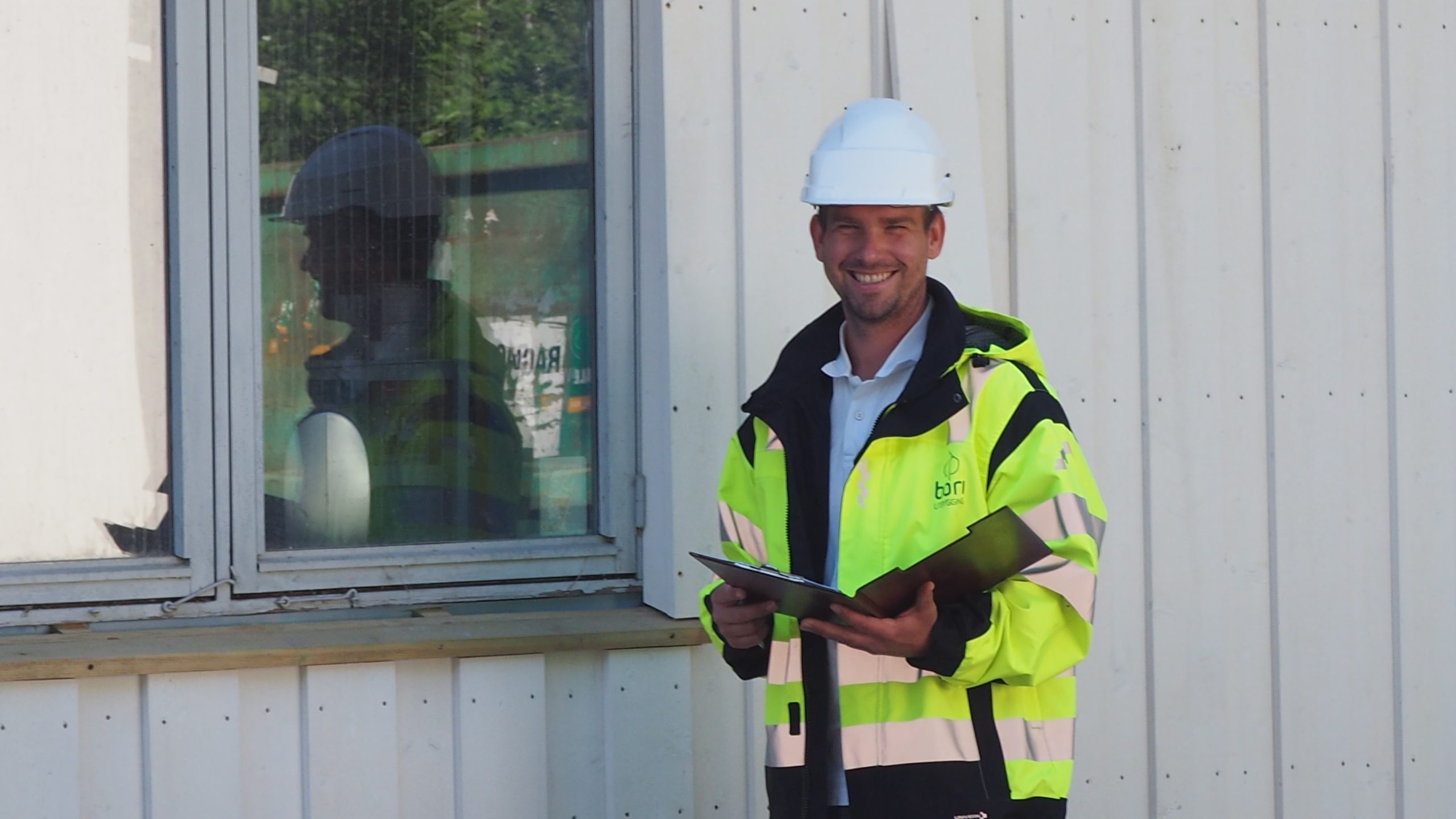 Teamleder i BORI Prosjekt, Stian Radford foran grønn busk med vernehjelm og gul arbeidsjakke