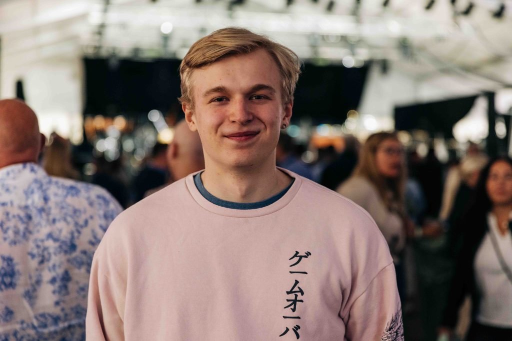Ung mann i rosa genser er på konsert, smiler mot kamera