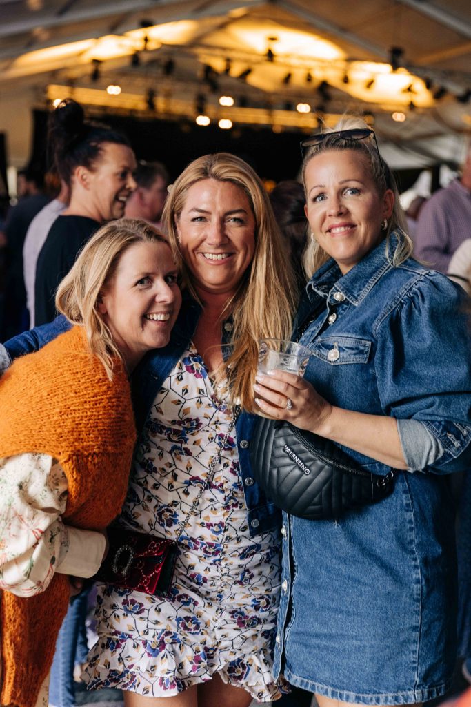 Tre venninner smiler mot kamera mens de koser seg på konsert