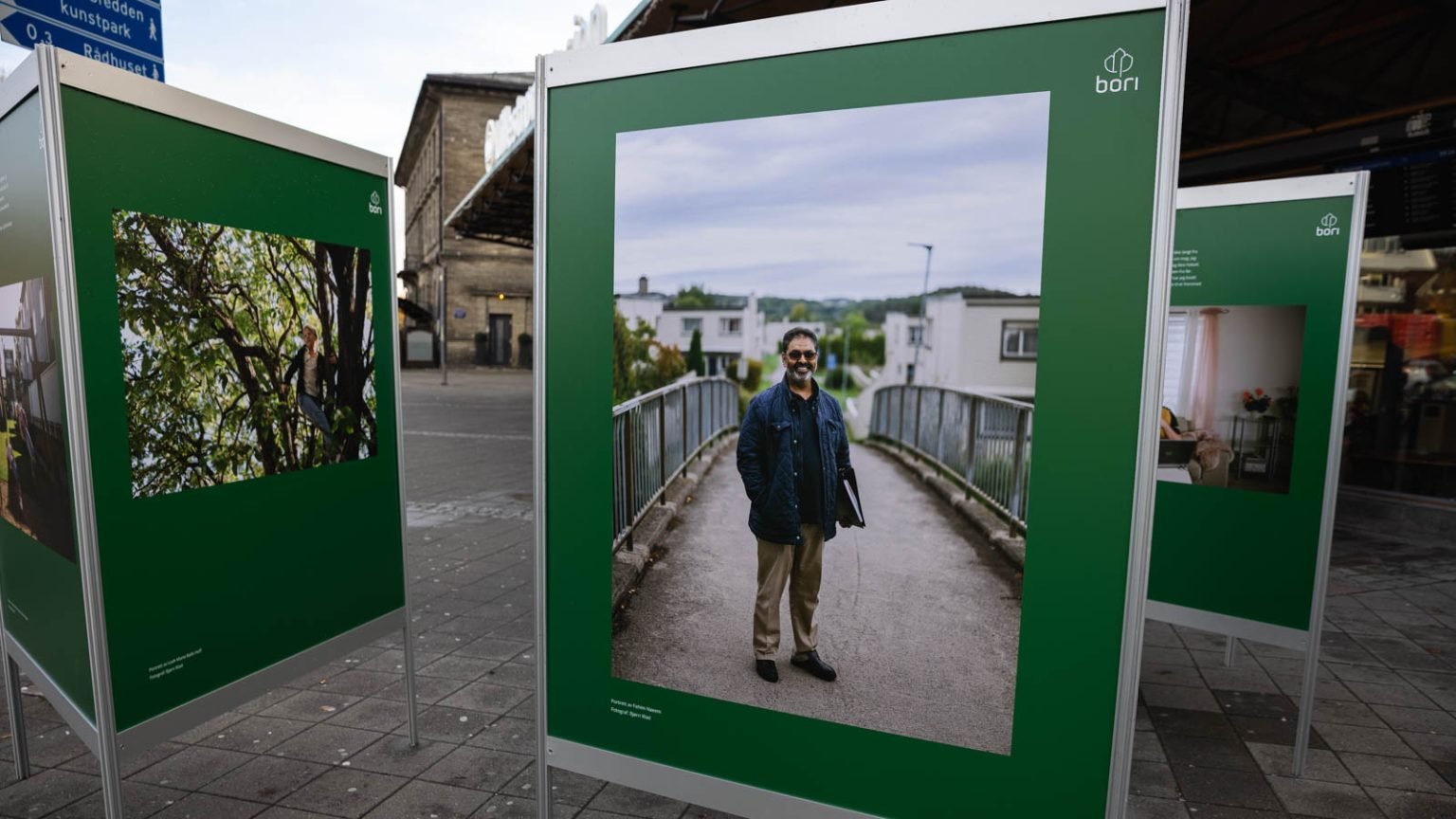Bilde av utstilling på grønne plakater, med en mann som står på bro med dokumenter under armen.