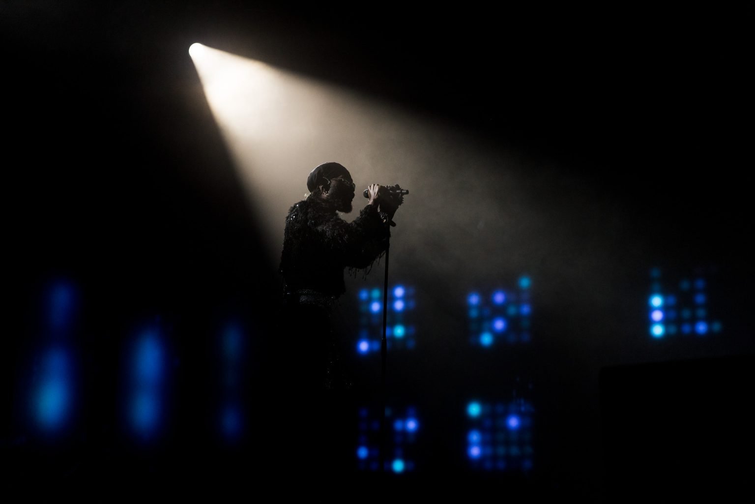 Artisten Arif på scenen som holder fast i mikrofonen og synger med spotlight på øvre delen av kroppen og sort bakgrunn med blå scenelys i veggene.