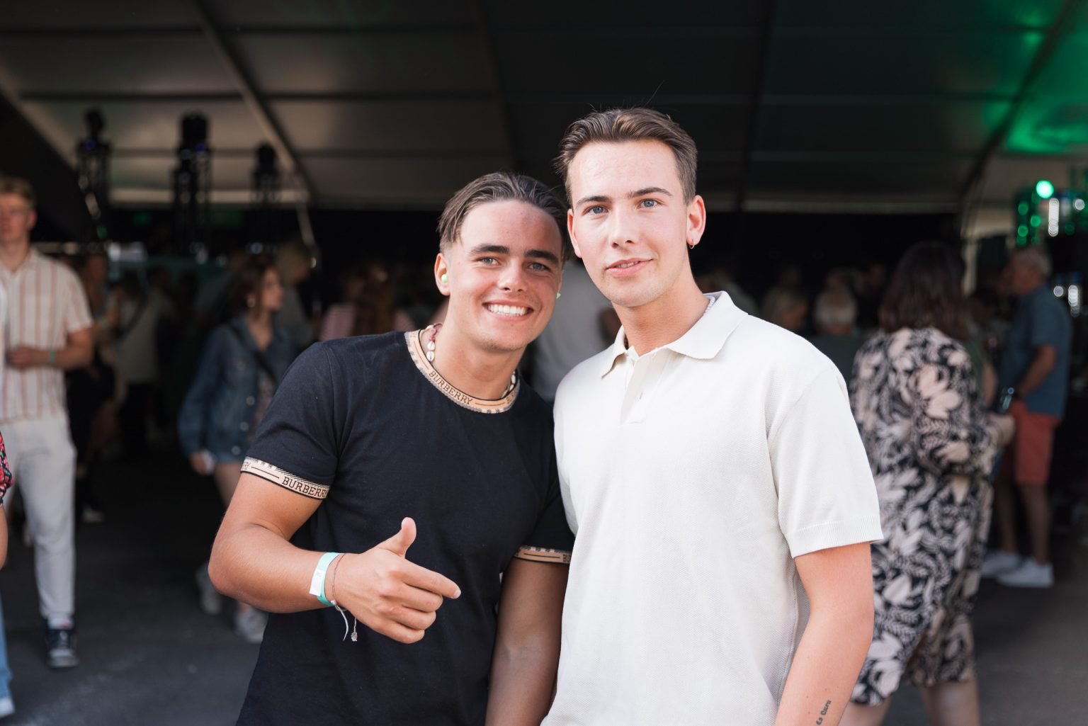 to gutter med brunt hår og hvit og sort t-skjorte som står ved konsert-området og smiler inn i kameraet.