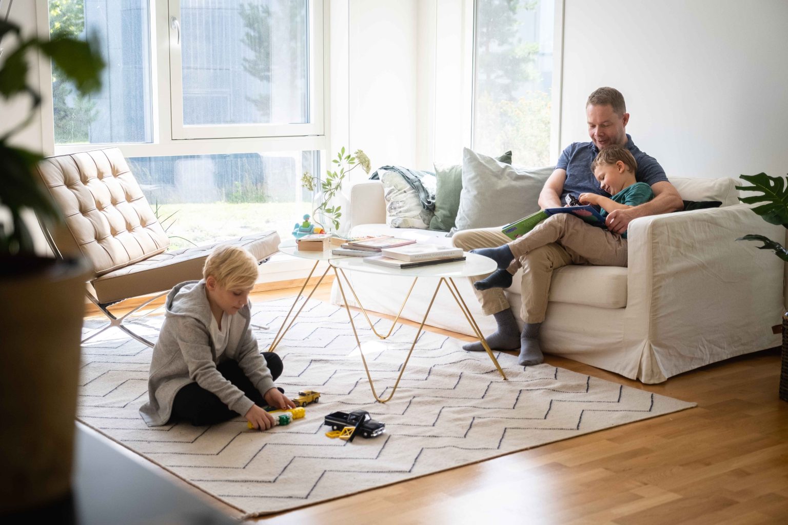Lyset flommer inn i den romslige stua. Pappaen leser bok sammen med en sønn, mens den andre leker på gulvet.
