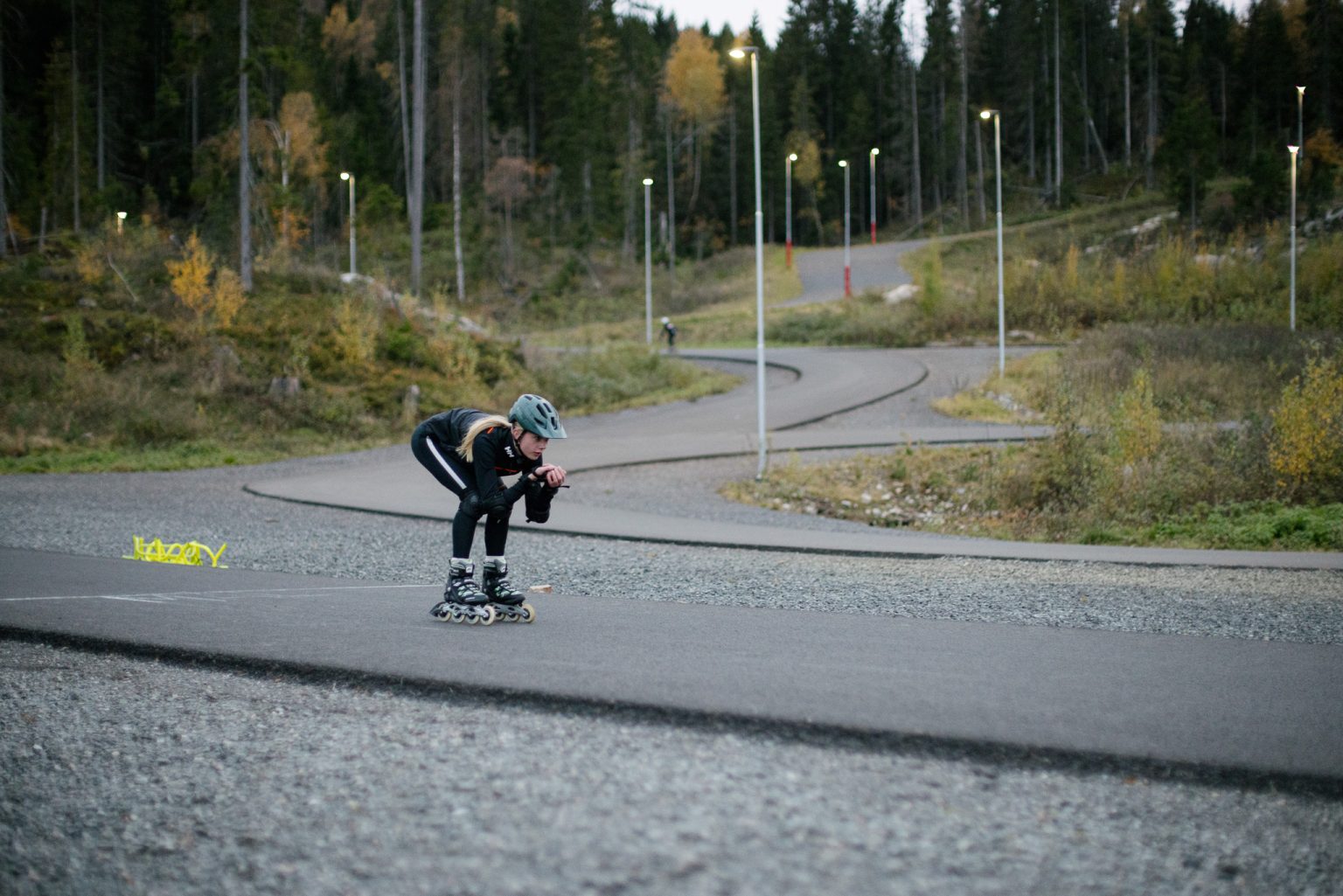 en jente i rollerbladesutstyr sitter på huk mens hun suser ned en asfaltbakke