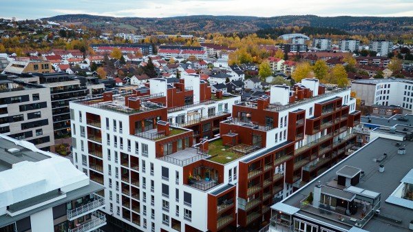 Luftfoto av et moderne urbant område med fleretasjes bolig- og kommersielle bygninger, kryssende gater og høstfargede trær i det fjerne.