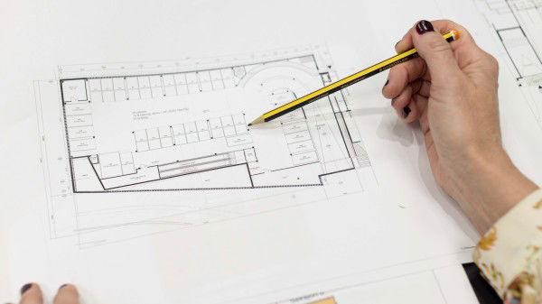 En person med blyant går gjennom en arkitekttegning på et hvitt ark og forbereder seg på å gjøre eiendom klar for salg.