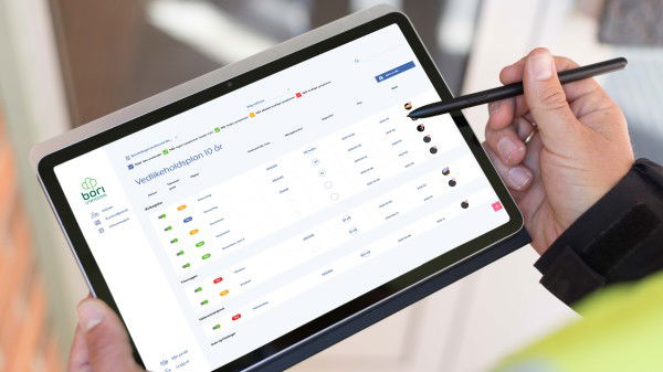 En person holder et nettbrett med en penn som viser en digital sjekkliste eller et arbeidsflytgrensesnitt med ulike statusindikatorer og oppgaveinformasjon knyttet til grønne rehabiliteringsprosjekter.